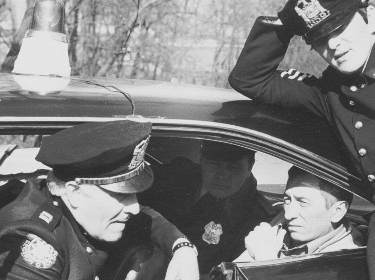 Images tirée du film policier polonais "Les Ennuis Sont Ma Spécialité". On peut y voir 3 policiers et un homme. Deux de ces personnages se trouvent dans une voiture de police.