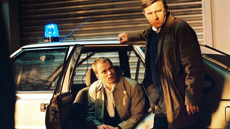 Image tirée de la série policière polonaise "Flic". On peut y voir une homme dans une voiture et un homme debout à côté.